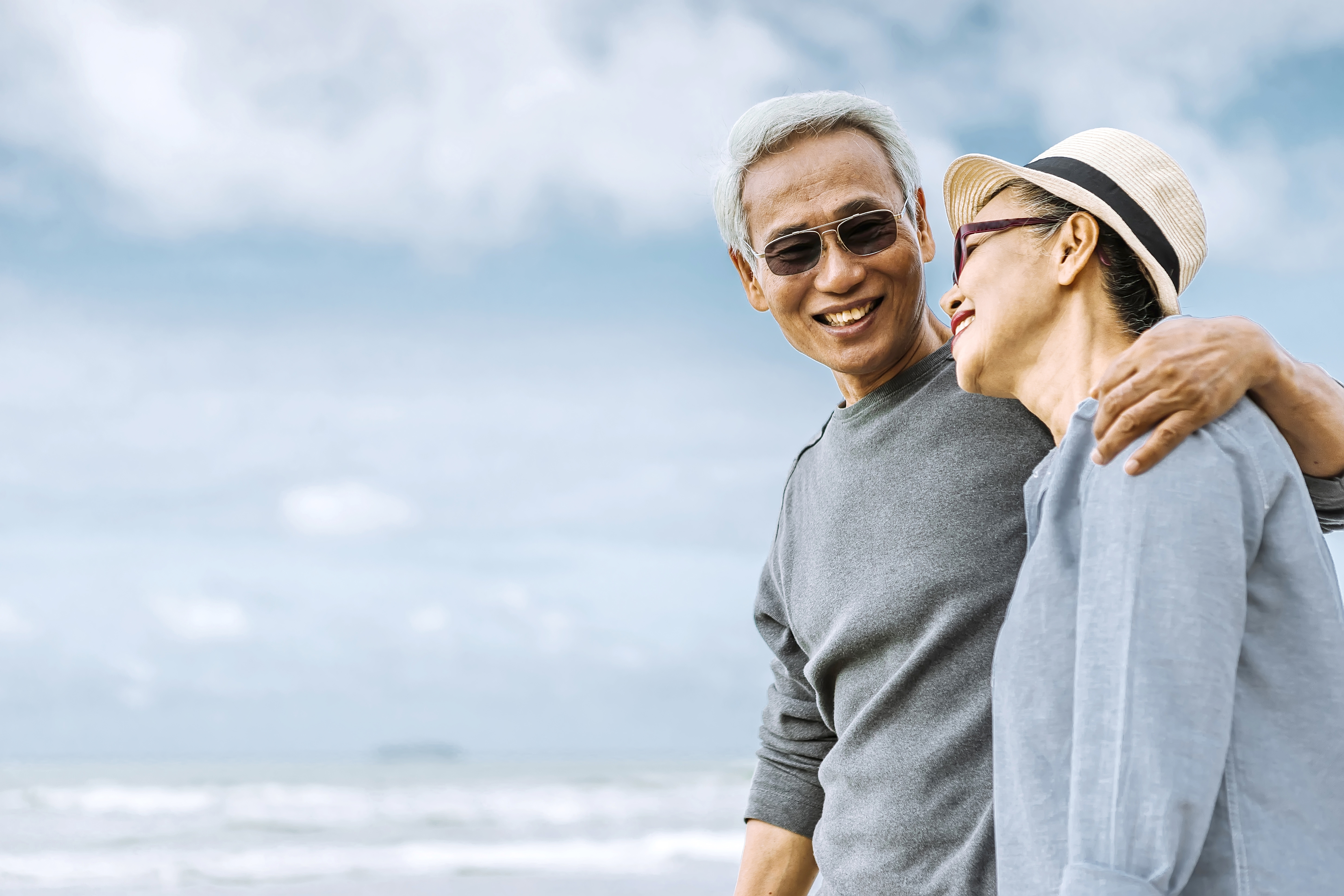 Two smiling people embrace against a cloudy sky