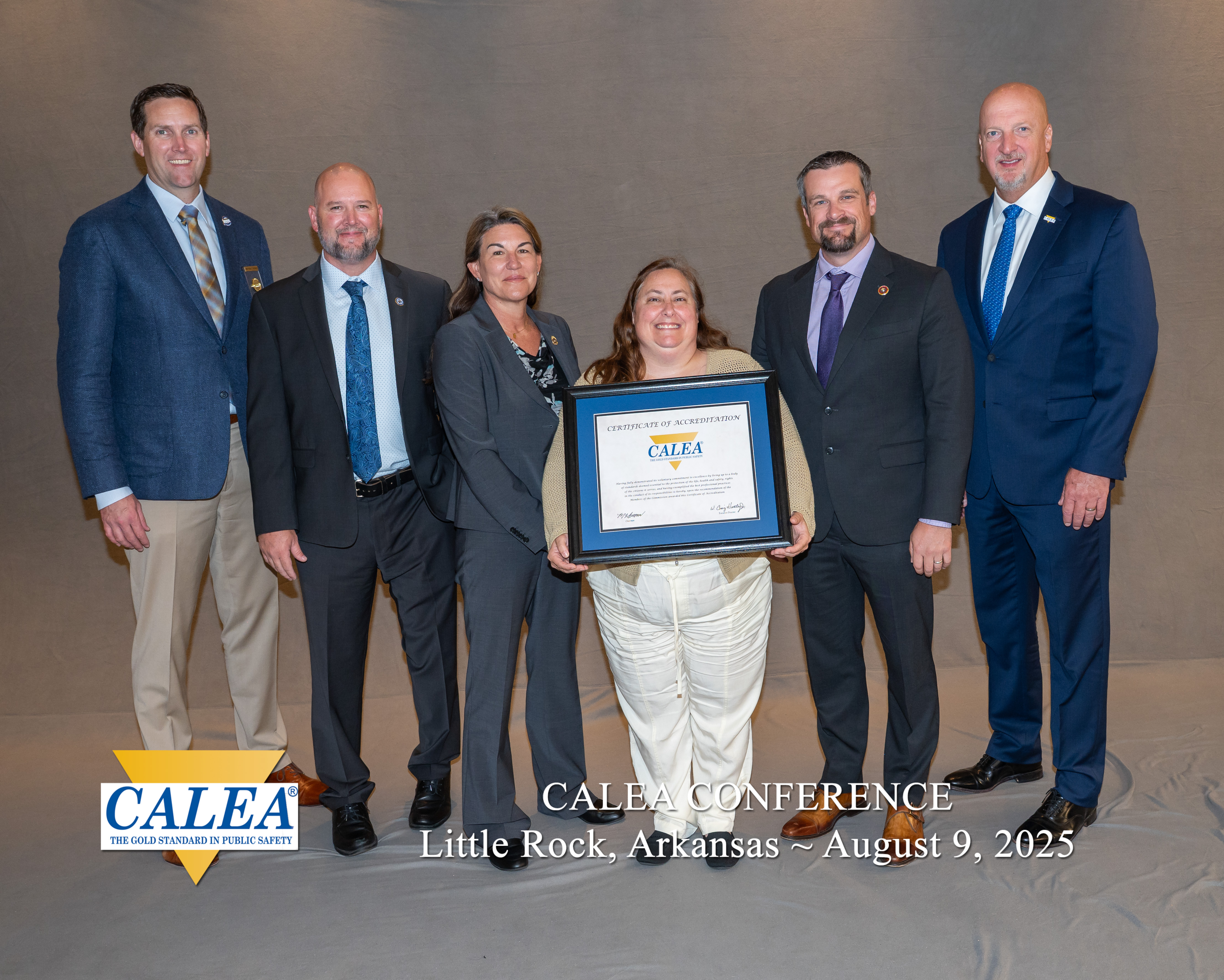 Six smiling people with a woman in the middle holding a CALEA certificate of accreditation